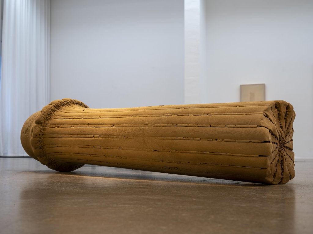 A 3D-printed sand sculpture rests on a concrete floor with horizontal ridges and a starburst pattern on the right end.