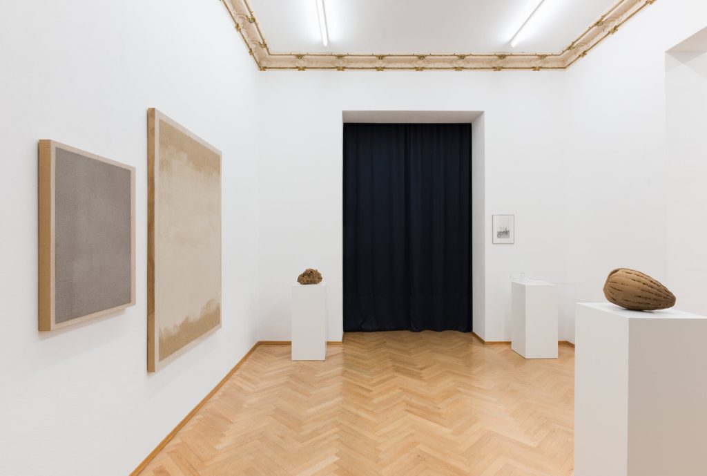 Three 3D-printed sand sculptures sit on white pedestals in an art gallery with herringbone wood flooring and two framed artworks on the wall.