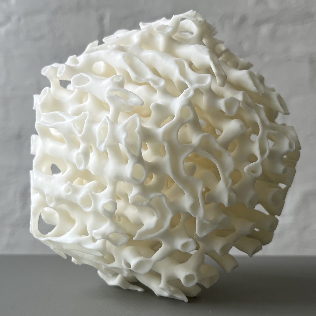 A white 3D printed resin polyhedron with porous structures sits on a gray surface.
