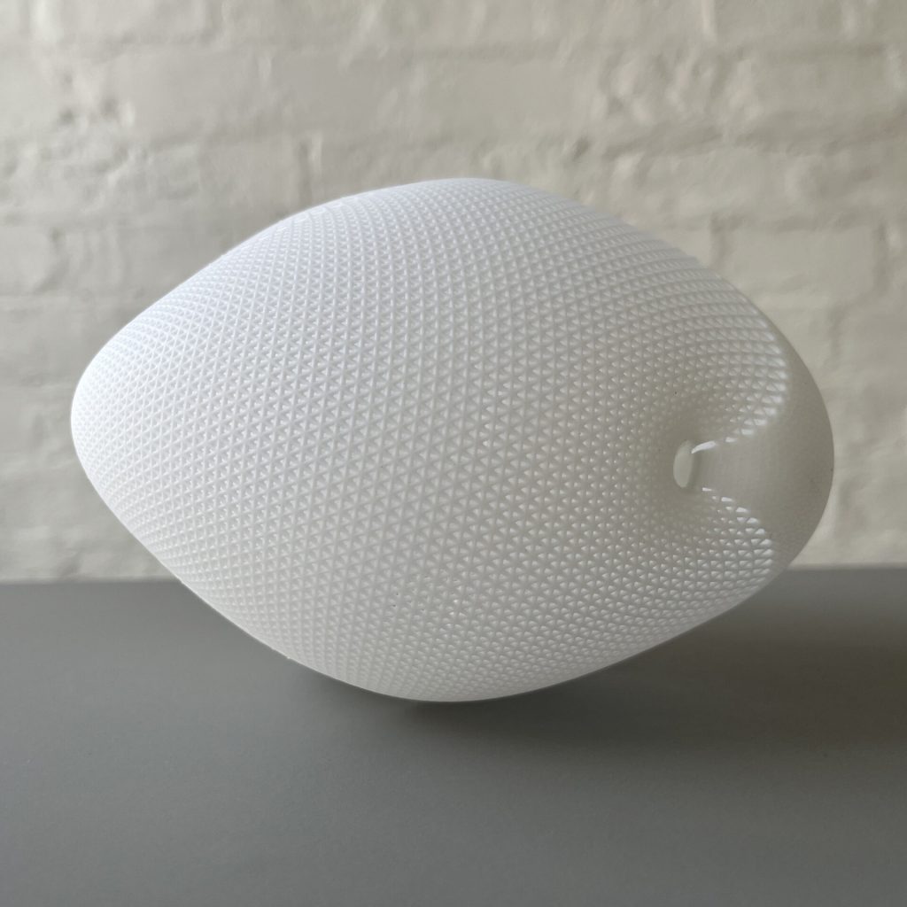 A white, 3D-printed resin object with a textured surface sits on a gray surface against a brick wall.