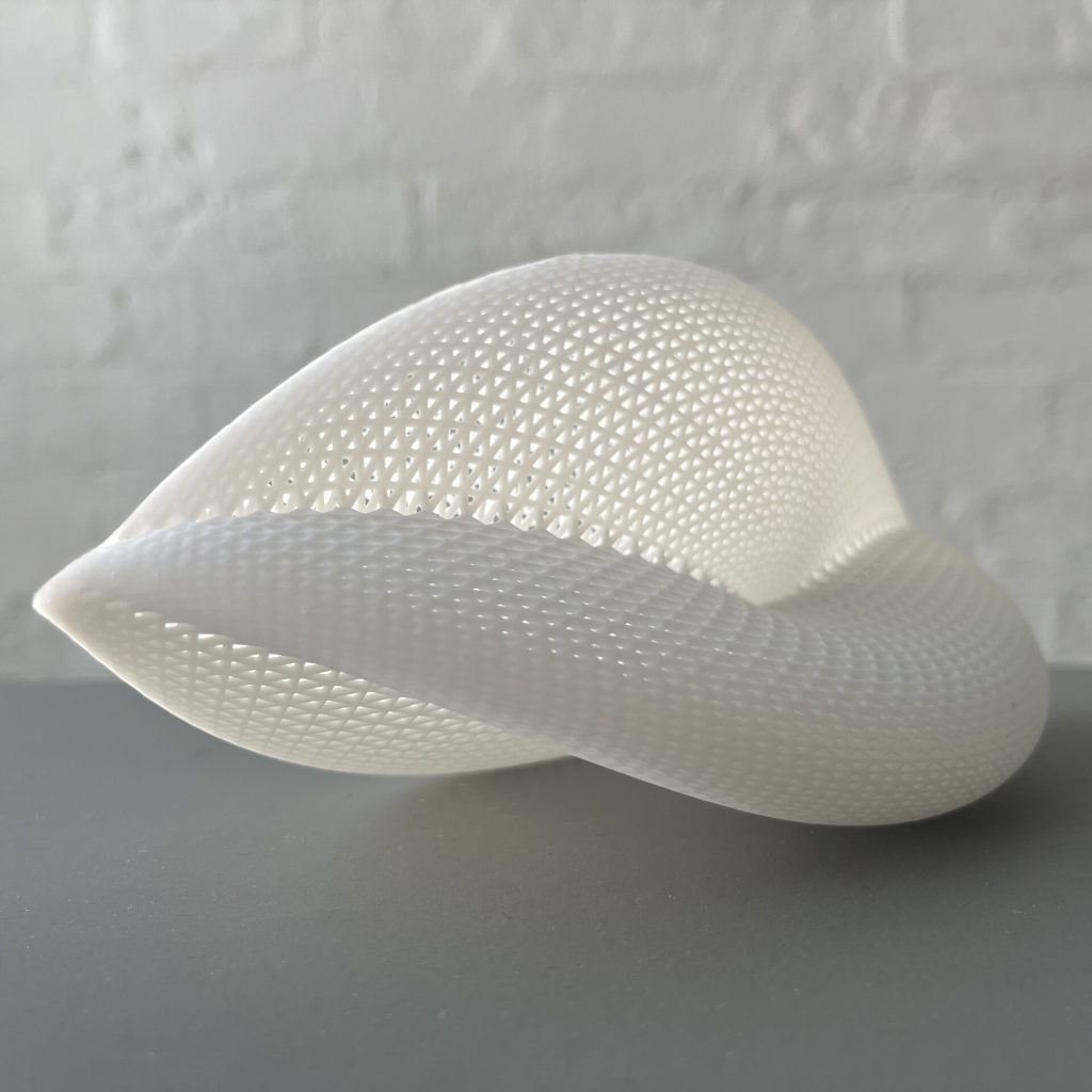 A white, 3D-printed resin object with a lattice pattern sits on a gray surface against a brick wall.
