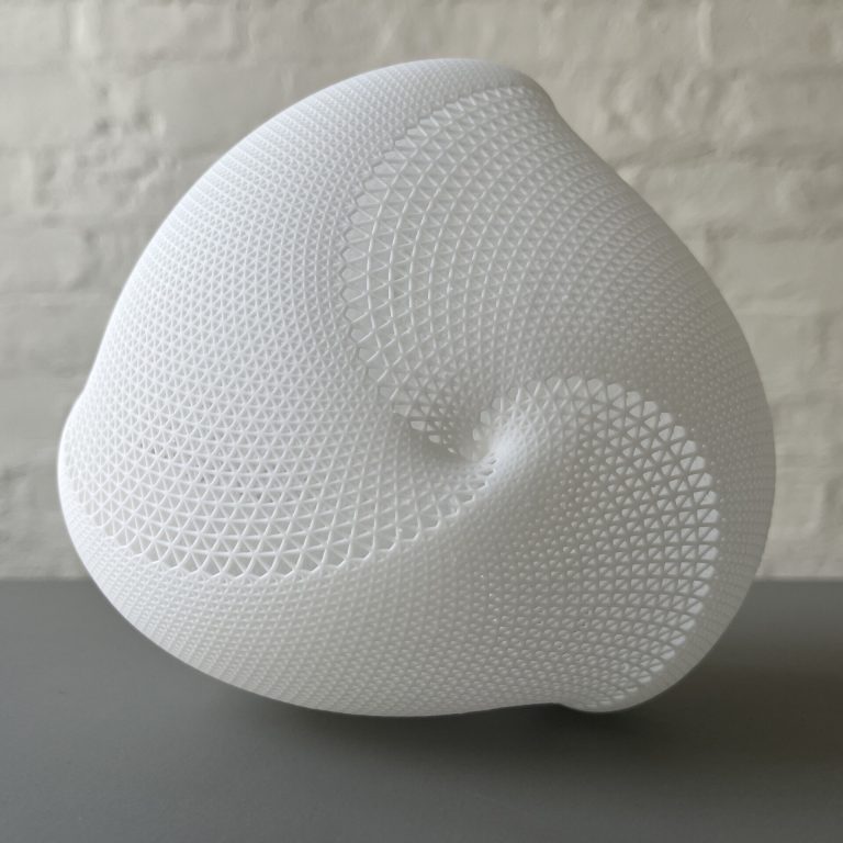 A white 3D printed resin globular form with a lattice pattern sits on a gray surface.