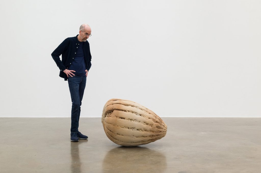 A man stands beside an enlarged, 3D-printed sand sculpture in a gallery space.