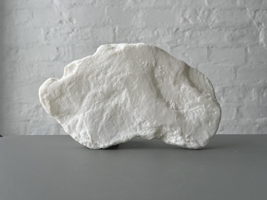 A white, irregularly shaped object made of 3D-printed resin sits on a gray surface against a textured wall.