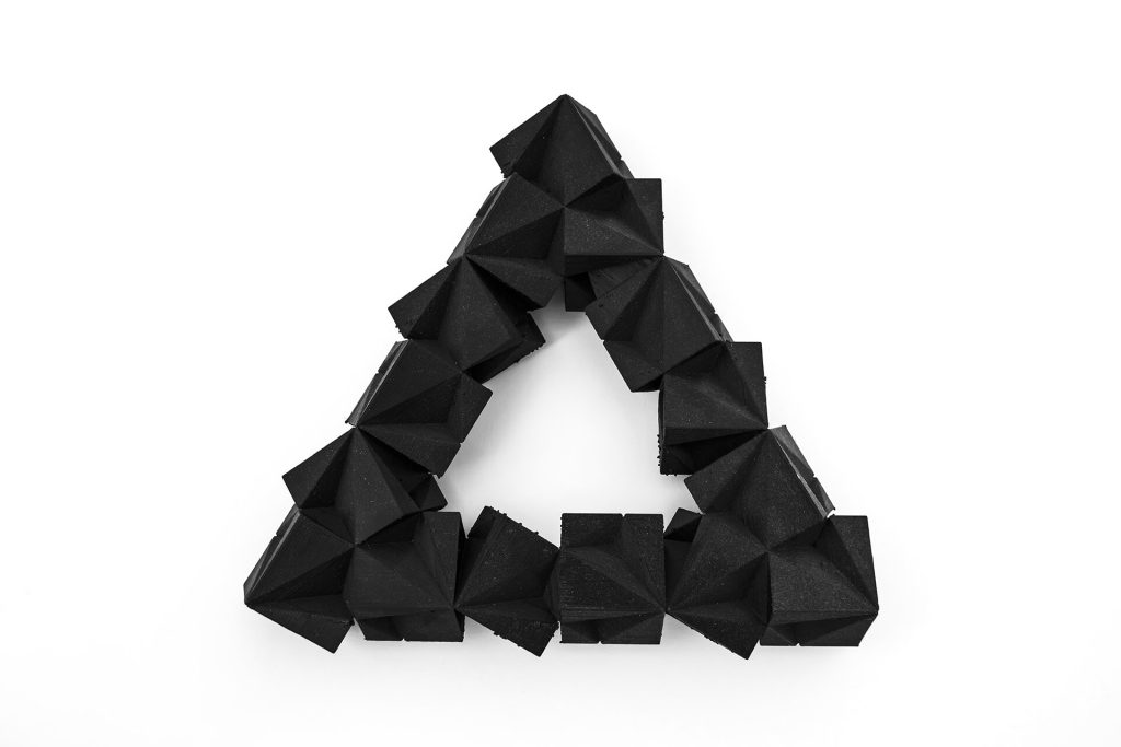 A black, 3D-printed resin triangle made of modular SuperCube Elements sits on a white surface.