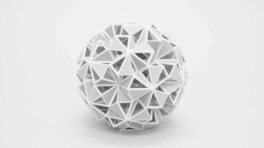 A white, 3D-printed resin sphere composed of interlocking triangular facets sits on a plain surface.