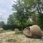 Three sand grain sculptures sit on a gravel path surrounded by trees and hedges.