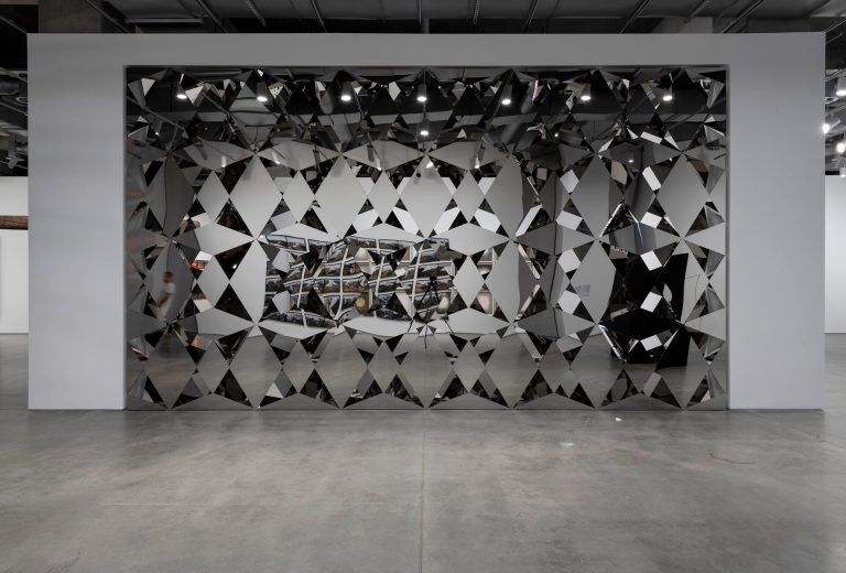 Diamond-shaped stainless-steel mirrors form a cubic wall partition with gaps revealing internal mirrors.