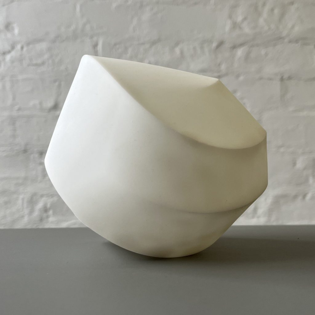 A white 3d printed resin polyhedron sits on a gray surface against a white brick wall.