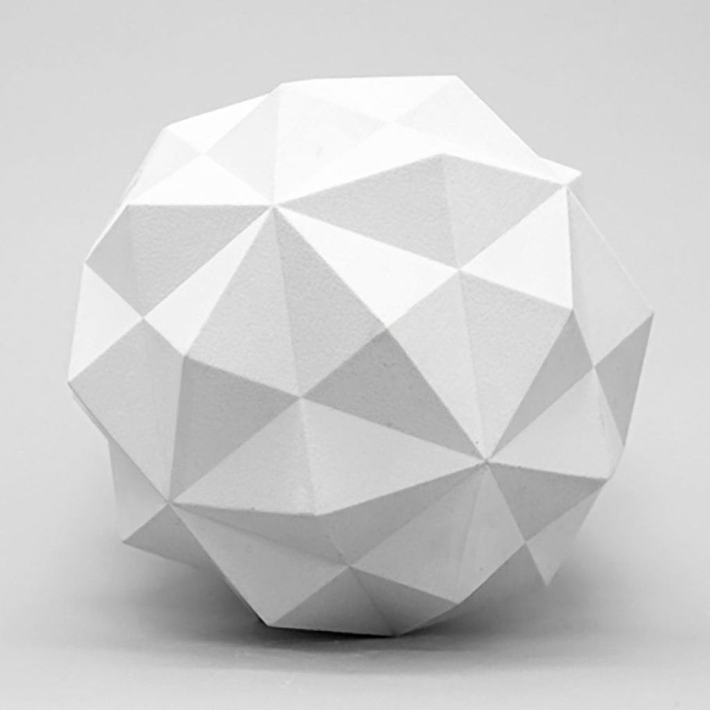 A white 3D printed resin polyhedron sits on a gray surface.