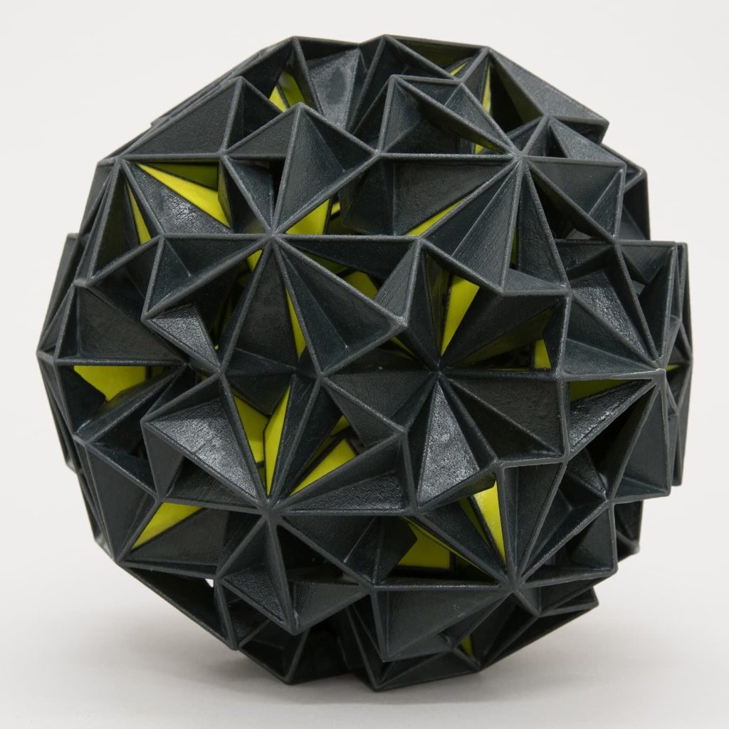A black 3D-printed plaster sphere with yellow interior shows a geometric pattern.