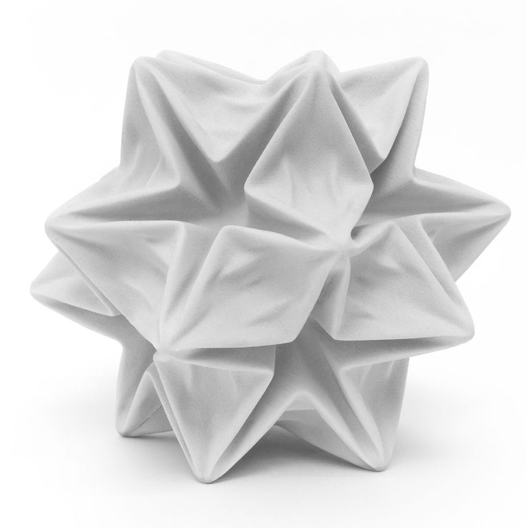 A white 3d printed resin stellated polyhedron with deformed facets sits on a white surface.