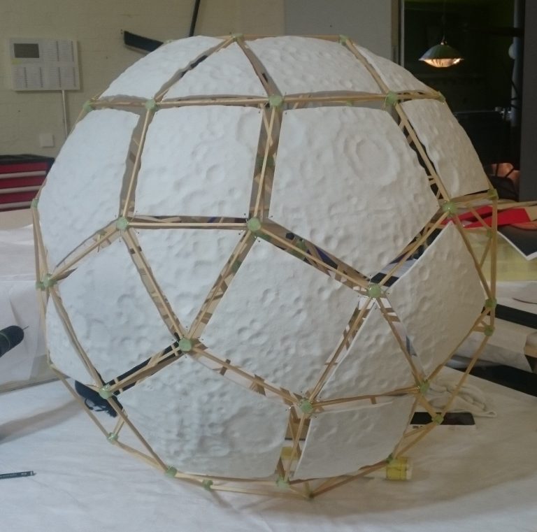 A wooden frame holds white textured panels in a spherical polyhedron shape.