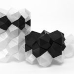Black and clear 3D printed resin polyhedra interlock in geometric clusters on a white surface.