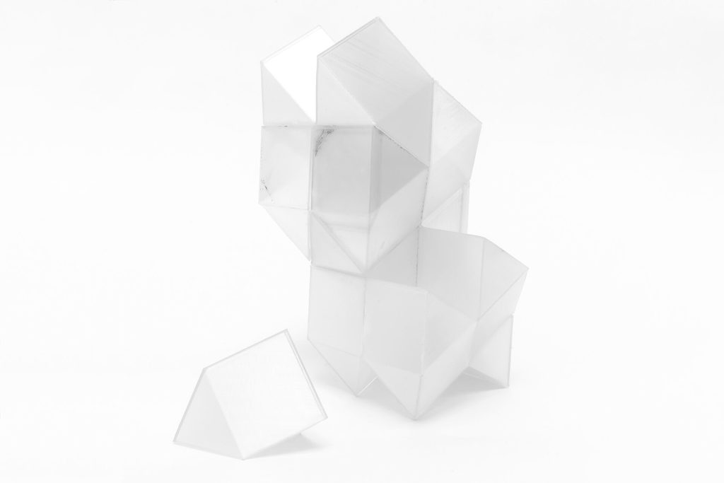 A stack of 3d printed resin polyhedra sits on a white surface with one piece detached.