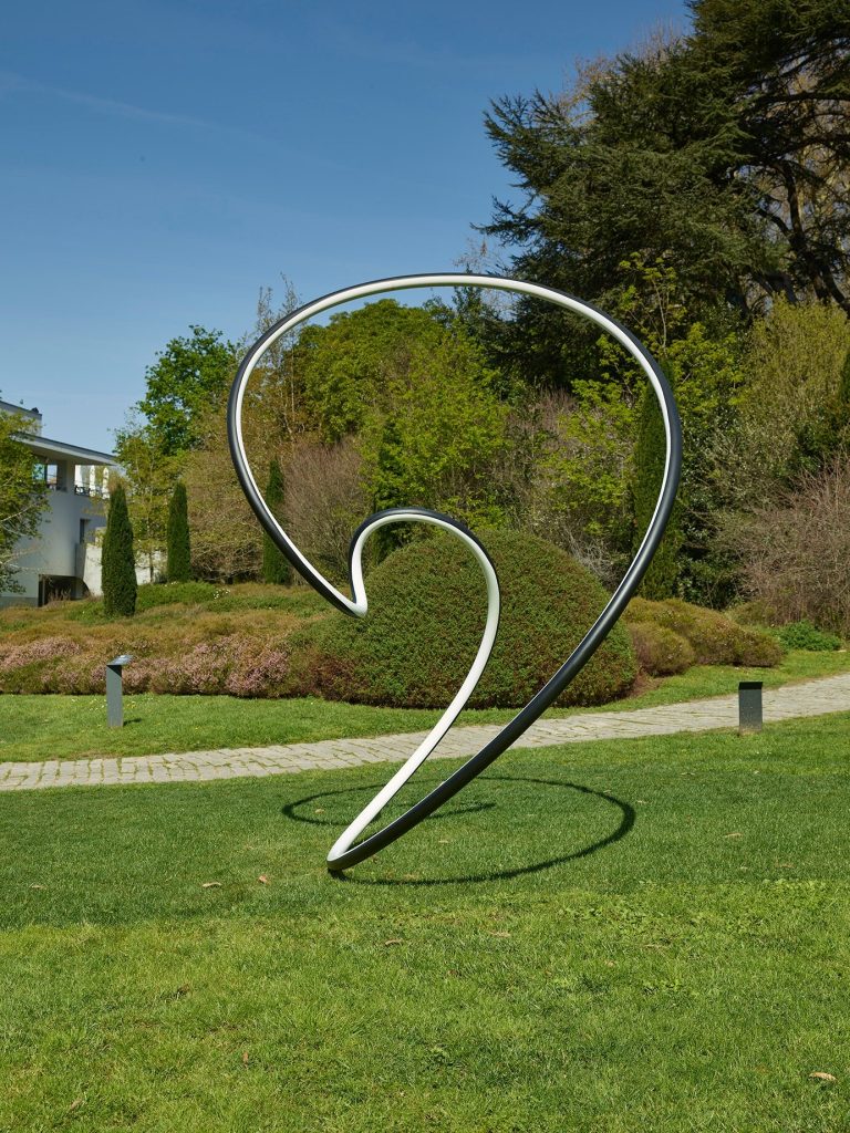 A black and white stainless steel Clelia curve stands on a lawn.