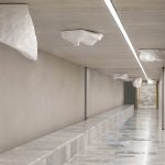 Seven Carrara marble blocks hang from the ceiling of a concrete tunnel with a marble bench.