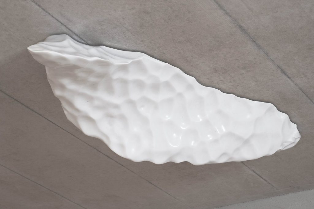 A white Carrara marble block with a textured surface hangs from a concrete ceiling.