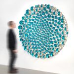 A stainless steel structure holds partially silvered glass spheres painted cyan and black on a white wall.