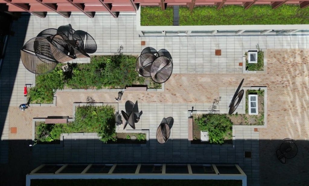 Eleven painted stainless steel and thermo-wood elements sit on a tiled courtyard at Woodhub.