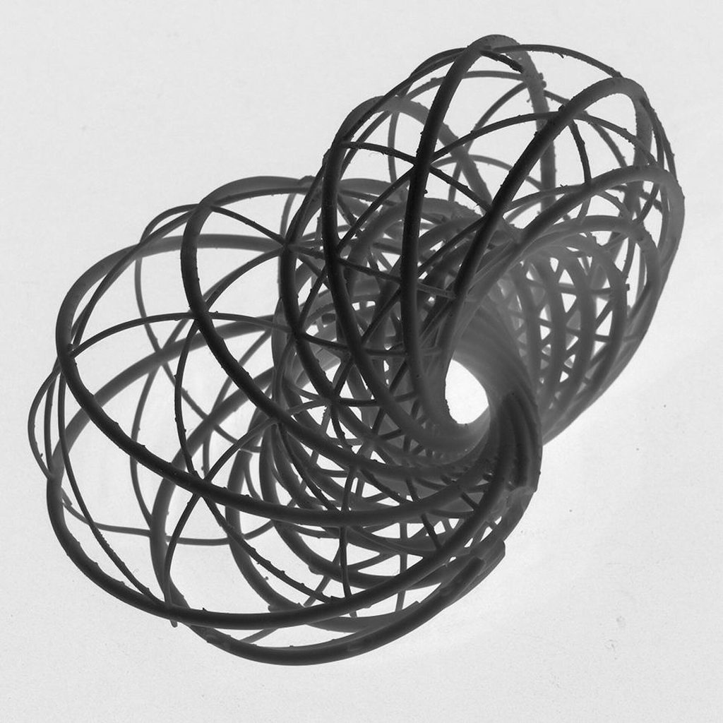 A 3D printed resin model of interlocking curves from Hopf Fibrations sits on a white surface.