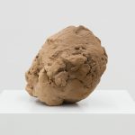 A 3D-printed sand sculpture with a rough, brown surface sits on a white plinth.