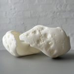 A white 3d printed resin object with porous surface sits on a gray surface.