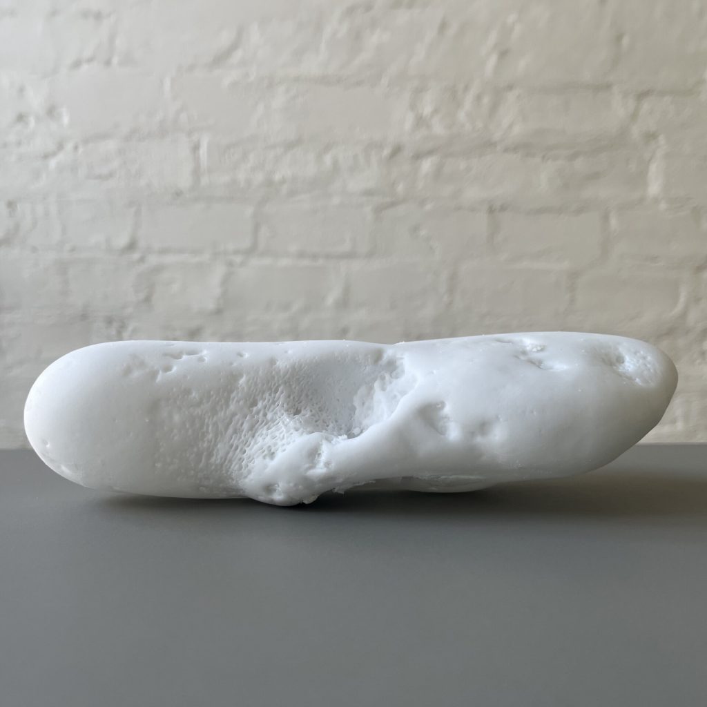 A white 3D printed resin object with a porous texture sits on a gray surface.
