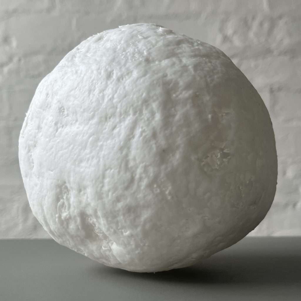 A white 3D printed resin sphere with a textured surface sits on a flat surface.