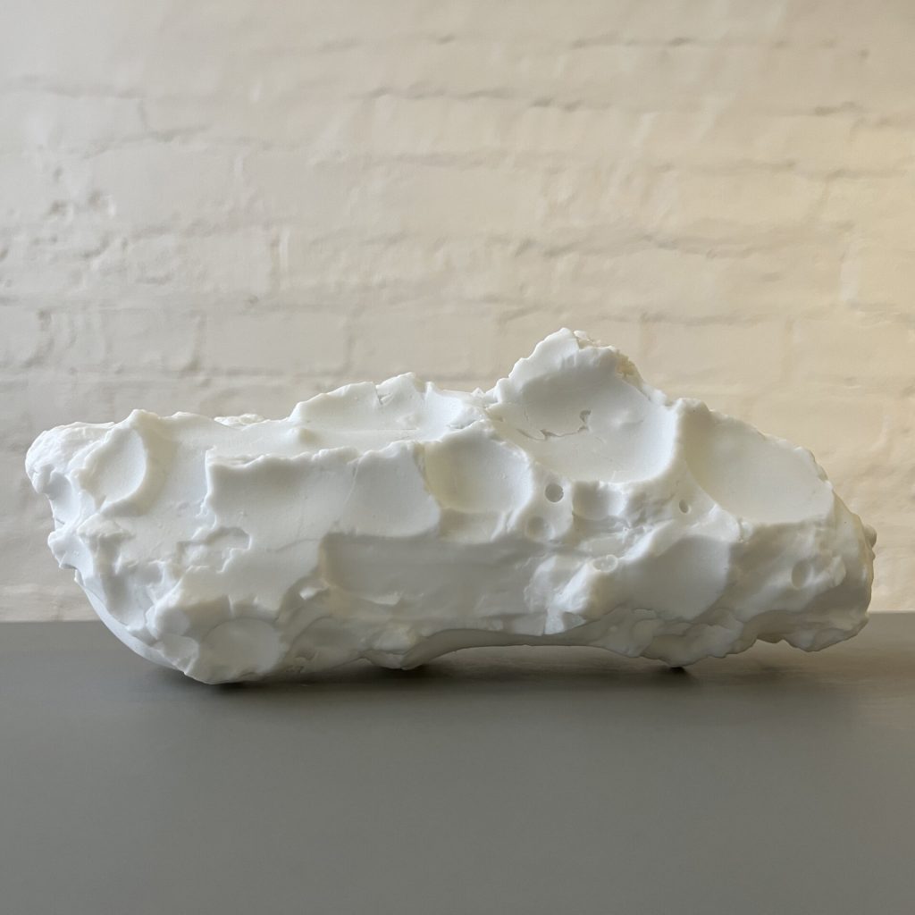 A white 3D printed resin object with an irregular, porous surface sits on a gray surface.
