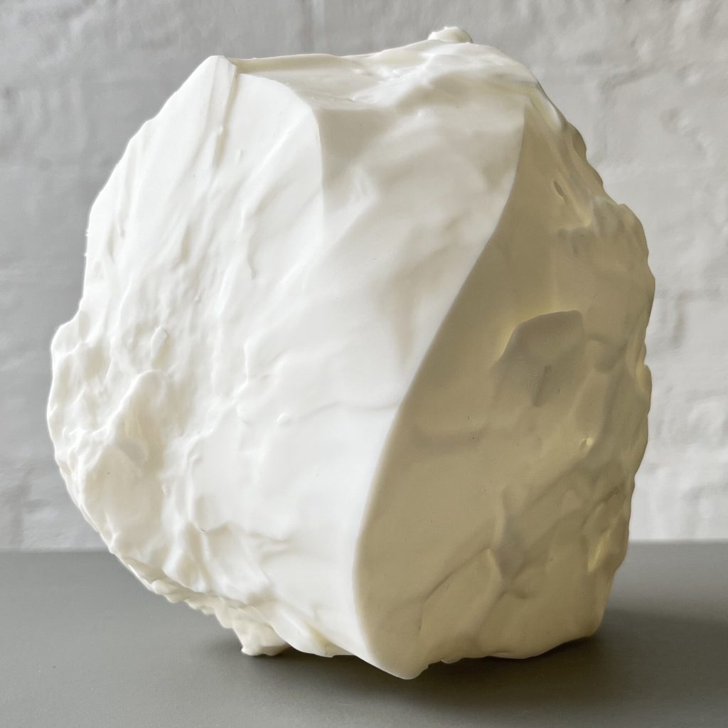 A white 3d printed resin object with sand grain topologies sits on a gray surface.