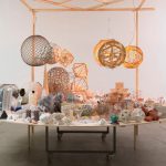 Geometric maquettes sit on a circular table, with wire spheres hanging from a wooden frame above.