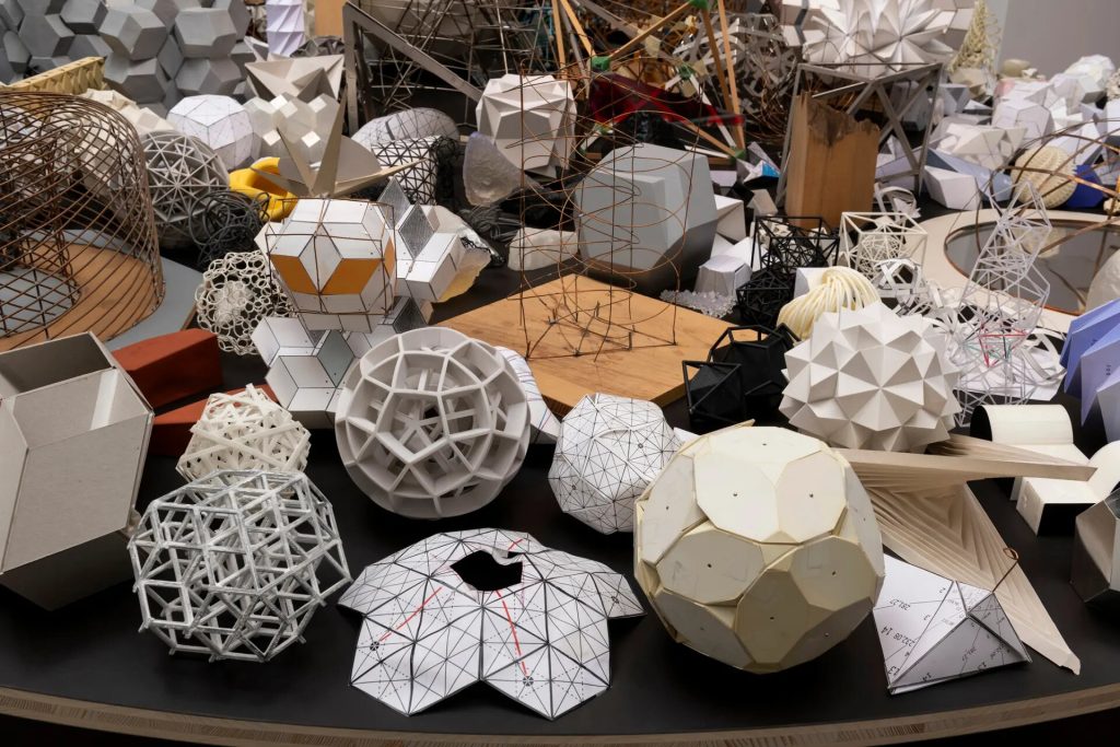 Geometric maquettes and prototypes sit on a circular table.