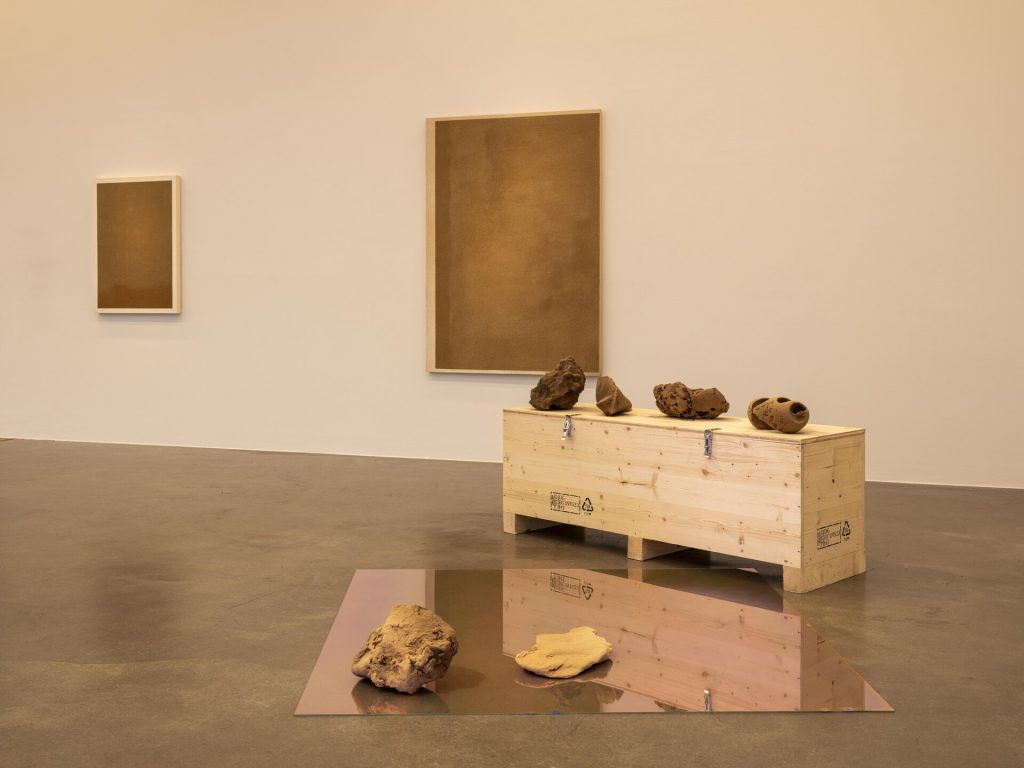 Sand paintings hang on the wall above 3D printed sand sculptures on a crate and mirror.