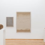Two 3D printed sand sculptures sit on white pedestals beside two framed sand works on a wall.
