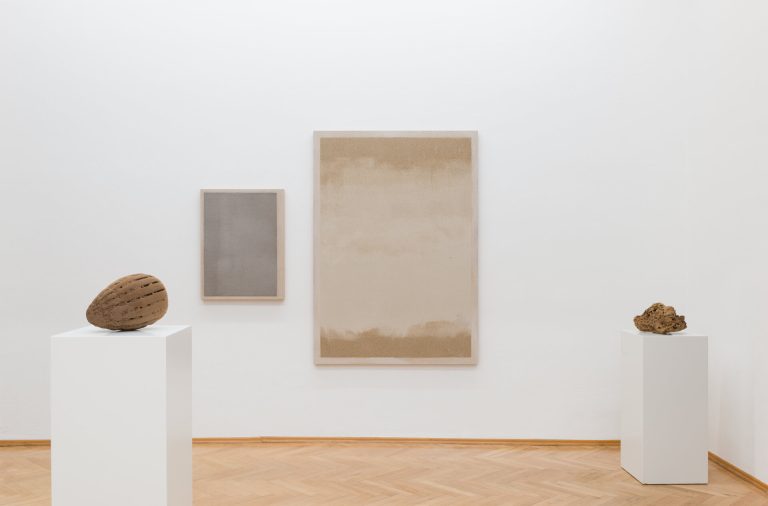Two 3D printed sand sculptures sit on white pedestals beside two framed sand works on a wall.