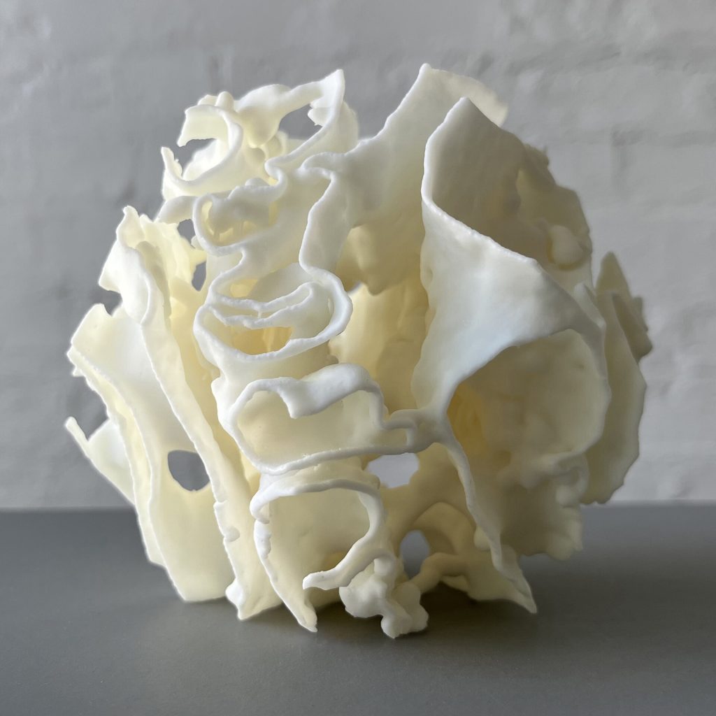 White 3D-printed resin Porouhedron #6 sits on a gray surface with curved walls and voids.