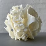 White 3D-printed resin Porouhedron #6 sits on a gray surface with curved walls and voids.