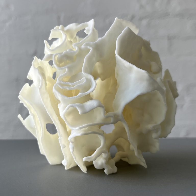 White 3D-printed resin Porouhedron #6 sits on a gray surface with curved walls and voids.