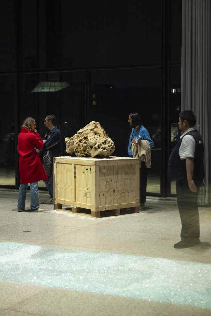 A 3d printed sand sculpture sits on a wooden crate while four people stand nearby.