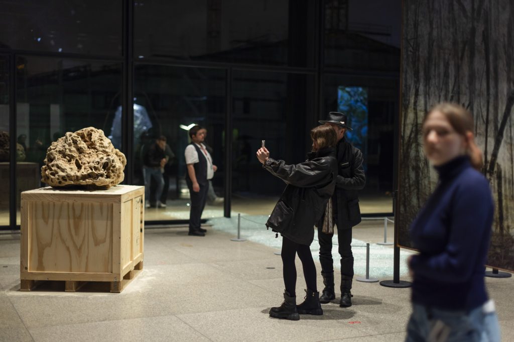 A 3d printed sand sculpture sits on a wooden crate while a couple takes a photo.