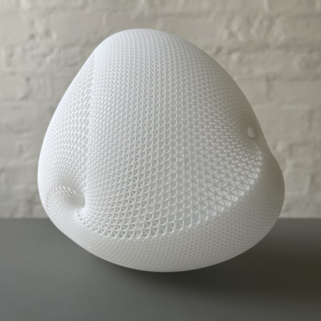 A white 3D printed resin object with a triangular mesh surface sits on a gray surface.