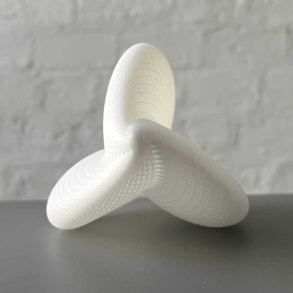 A white 3D printed resin object with three curved arms sits on a gray surface.