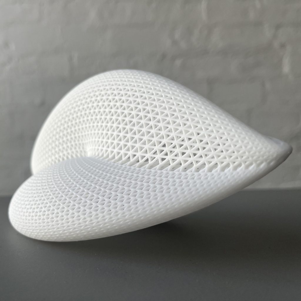 A white 3D printed resin hypergraph with a triangular mesh sits on a gray surface.
