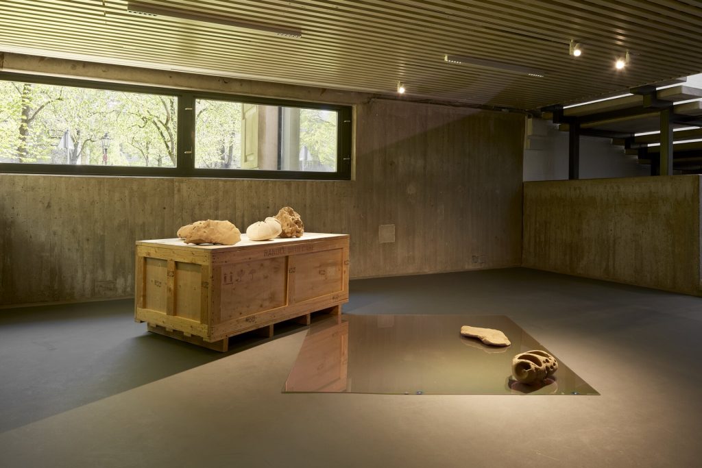 3d printed sand sculptures sit on a wooden crate and a glass sheet in a concrete room.