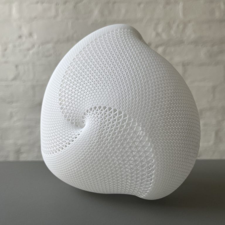 A white 3D printed resin object with a triangular lattice pattern and a central hole sits on a gray surface.