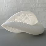 A white 3D printed resin shell with a triangular mesh pattern sits on a gray surface.