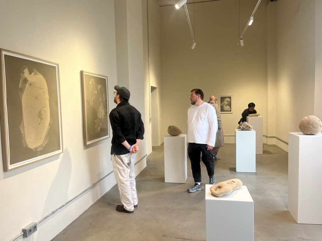 A gallery room holds framed charcoal drawings on the left wall and ash-soap forms on white plinths in the center.