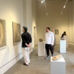 A gallery room holds framed charcoal drawings on the left wall and ash-soap forms on white plinths in the center.