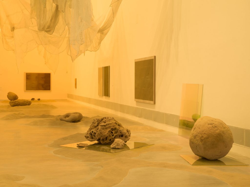 Sand covers the gallery floor, with 3D-printed sand sculptures on glass panels and sand paintings on the walls.